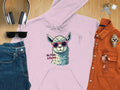 A flat lay image from Garment Graphics features a classic fit pink hoodie with a llama in funny sunglasses and the text No Prob-Llama, paired with blue jeans, black sunglasses, headphones, keys, a wristwatch, and an orange shirt with glasses.