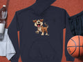 A playful black cartoon puppy hoodie from Garment Graphics rests on a red textured surface, perfect for a fun wardrobe. Nearby are essentials for dog lovers: a water bottle, white towel, black athletic shorts, and an orange basketball.