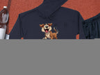 A playful black cartoon puppy hoodie from Garment Graphics rests on a red textured surface, perfect for a fun wardrobe. Nearby are essentials for dog lovers: a water bottle, white towel, black athletic shorts, and an orange basketball.