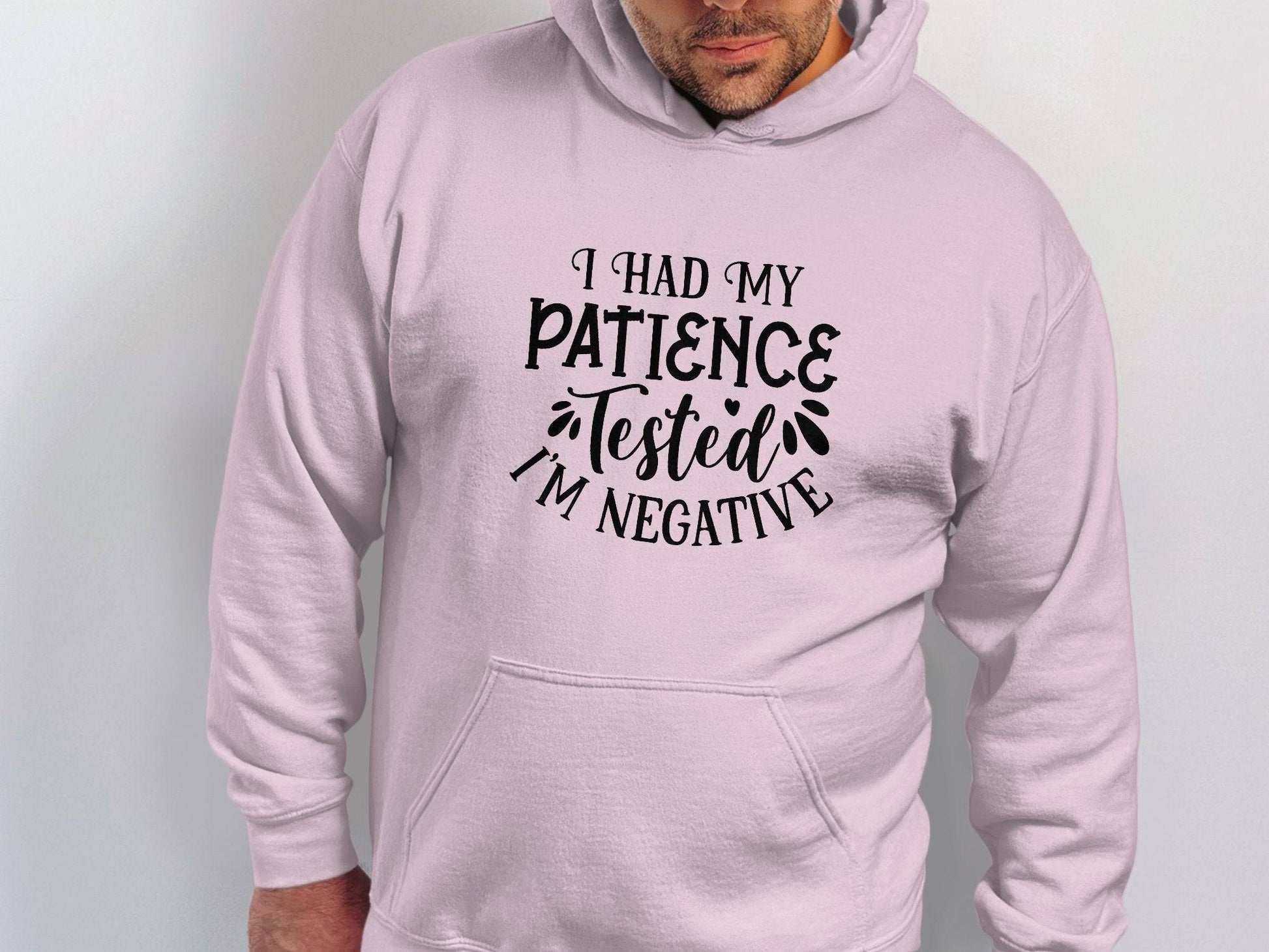 Someone is wearing a classic fit, light pink hoodie by Garment Graphics featuring I had my patience tested Im negative in black text, made from medium-heavy fabric for comfort.