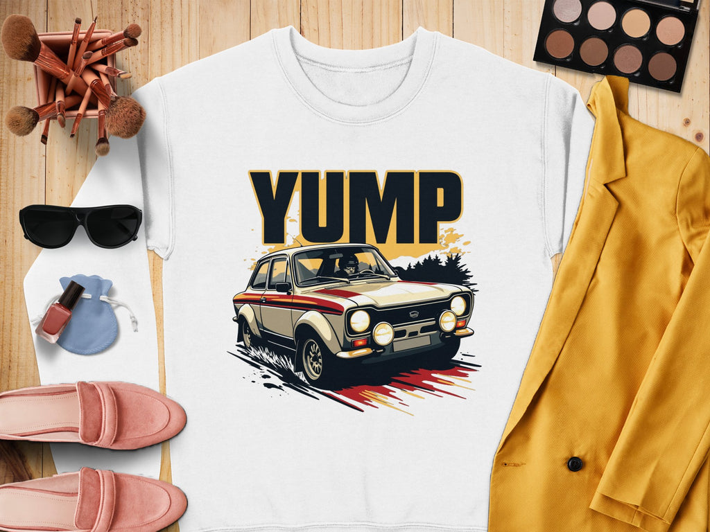A flatlay features a Garment Graphics white shirt with a rally car design and YUMP, paired with chic sunglasses, makeup brushes, an eyeshadow palette, pink loafers, nail polish, a yellow jacket, and an elegant jewelry pouch.