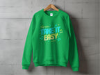 A Garment Graphics green sweatshirt hangs on a hanger against a gray wall, featuring the vibrant Take It Easy graphic in colorful lettering. Adorned with music notes and arrow designs, its unisex sizing ensures comfort for everyone.