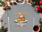 A Garment Graphics gray long-sleeve shirt showcases a fun pie character with whipped cream on a plate. The text Hot & Spicy appears above, and You Wanna a Piece of Me? is below. Available in unisex sizing, its styled with Christmas decor and a cup of beverage.