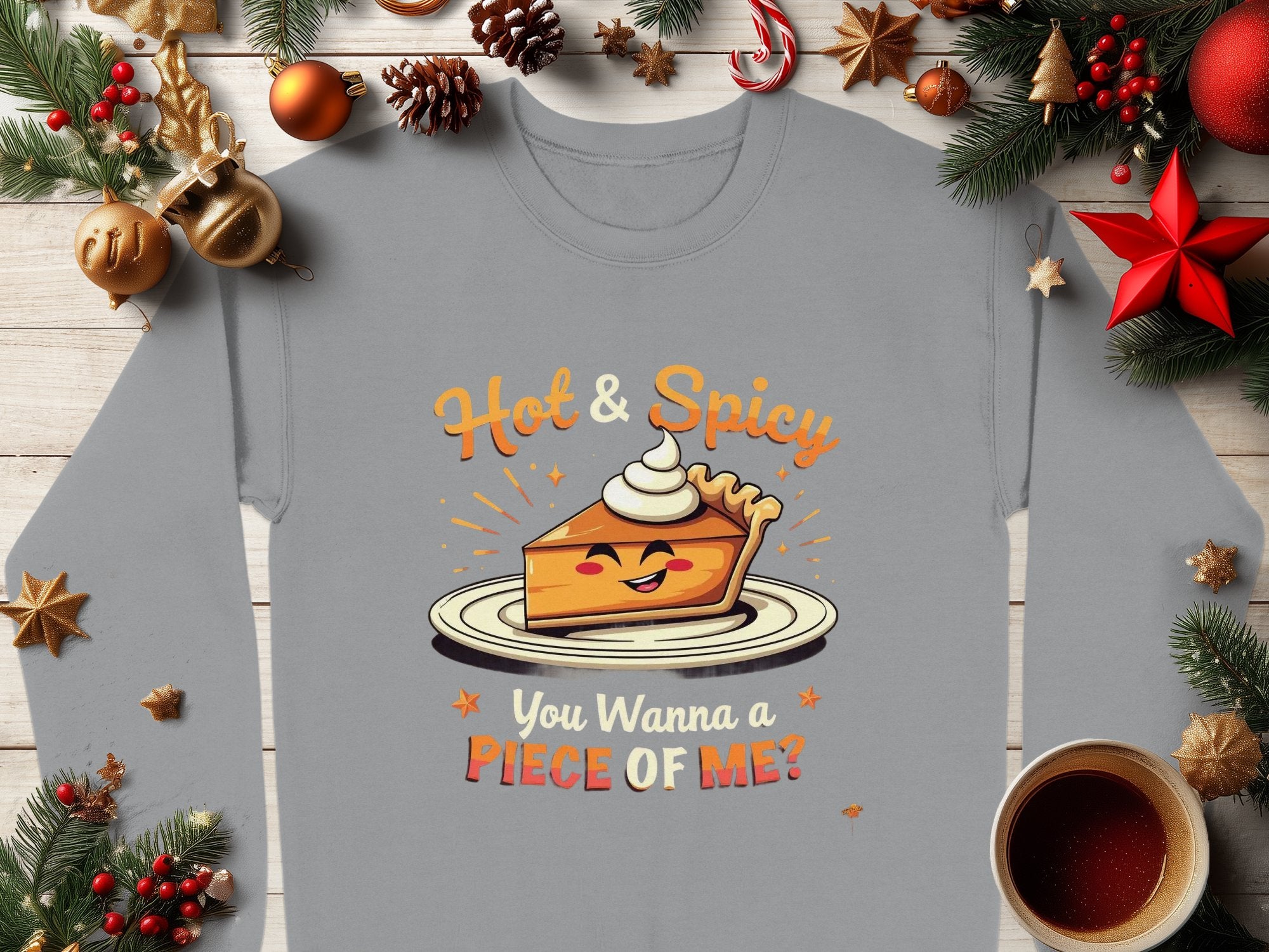 A Garment Graphics gray long-sleeve shirt showcases a fun pie character with whipped cream on a plate. The text Hot & Spicy appears above, and You Wanna a Piece of Me? is below. Available in unisex sizing, its styled with Christmas decor and a cup of beverage.