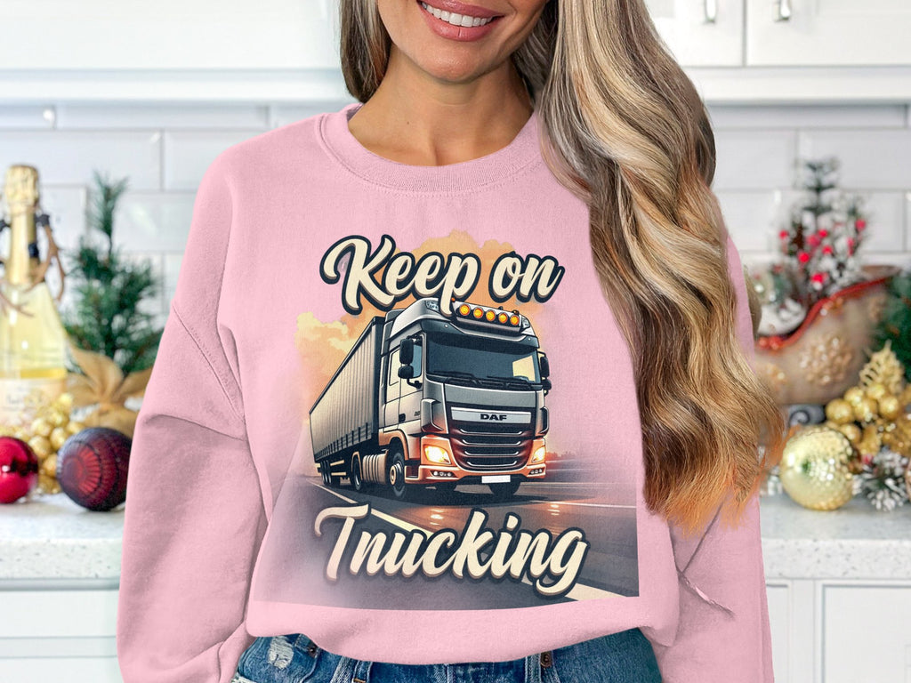 A person with long blonde hair stands indoors wearing a Garment Graphics sweatshirt featuring a whimsical truck and Keep On Trucking. Holiday decor surrounds them against white tiles and cabinets. This cozy unisex piece is perfect for everyone.