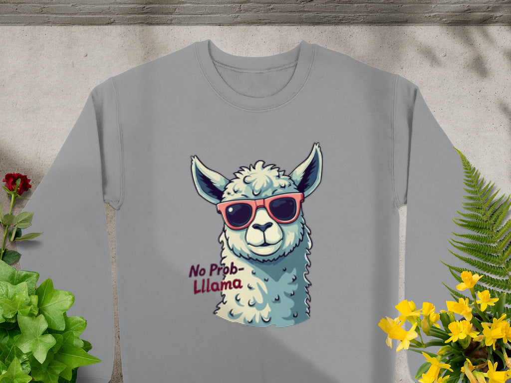 The Garment Graphics No Prob-Llama sweatshirt in gray features a playful llama with pink sunglasses and No Prob-llama text. It has a unisex fit and is styled against a concrete background with green and yellow plants.