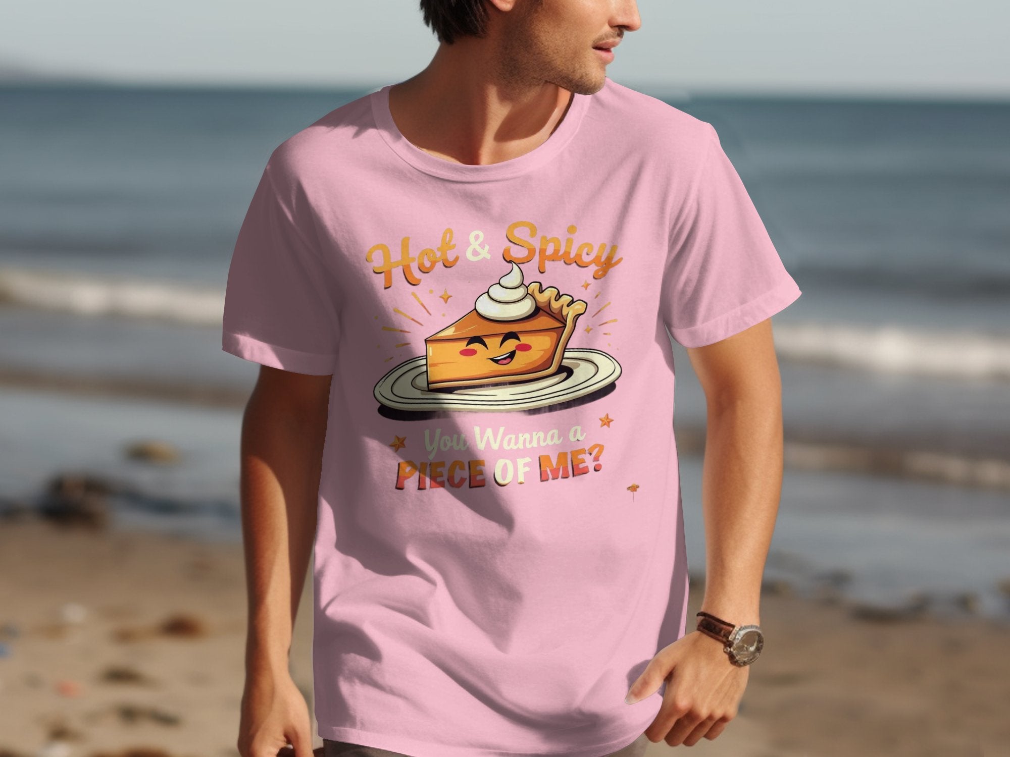 A person wearing a Garment Graphics pink T-shirt with the Hot & Spicy Pie Design and the text You Wanna a Piece of Me? walks along a beach, sand and waves in the background.