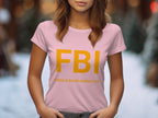 The Garment Graphics pink T-shirt, ideal as a gag gift, features large yellow FBI letters and humorous Female Boob Inspector in smaller print. Designed for women, it offers a comfy fit perfect for the outdoors, with a blurred background suggesting an open-air environment.