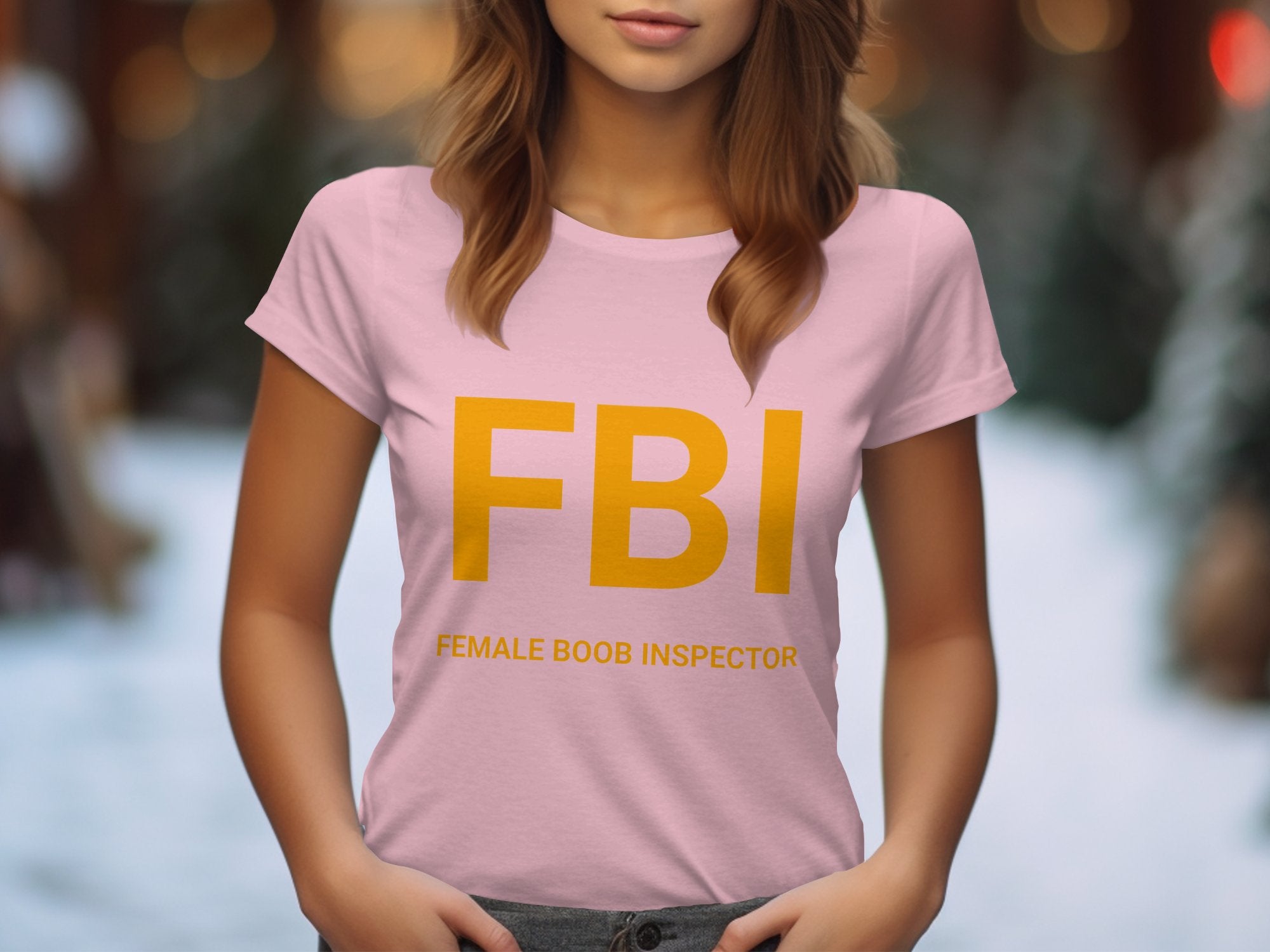 The Garment Graphics pink T-shirt, ideal as a gag gift, features large yellow FBI letters and humorous Female Boob Inspector in smaller print. Designed for women, it offers a comfy fit perfect for the outdoors, with a blurred background suggesting an open-air environment.