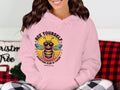 A person is in a Garment Graphics Summertime Edition Bee Yourself Hoodie, featuring a bee with sunglasses and the motto Bee Yourself, Everyone Else is Taken. Seated on a couch with a red and black plaid blanket, they effortlessly combine comfort and style.