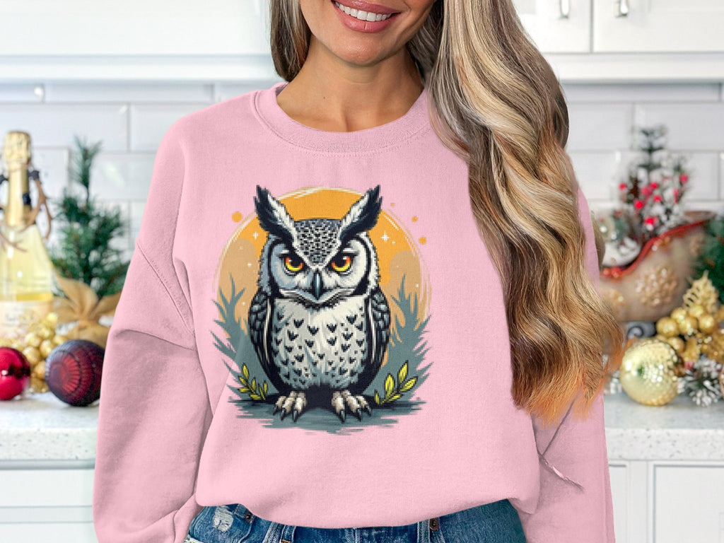 A woman with long, wavy blonde hair wears a unisex pink sweatshirt from Garment Graphics, featuring an enchanting owl design with piercing eyes and foliage. She is in a festive kitchen adorned with a decorated tree and seasonal decor.