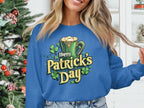 A person wearing a vibrant blue Garment Graphics sweatshirt featuring a Happy St. Patricks Day mug graphic stands before a decorated Christmas tree, surrounded by a white shelf adorned with plants and ornaments.