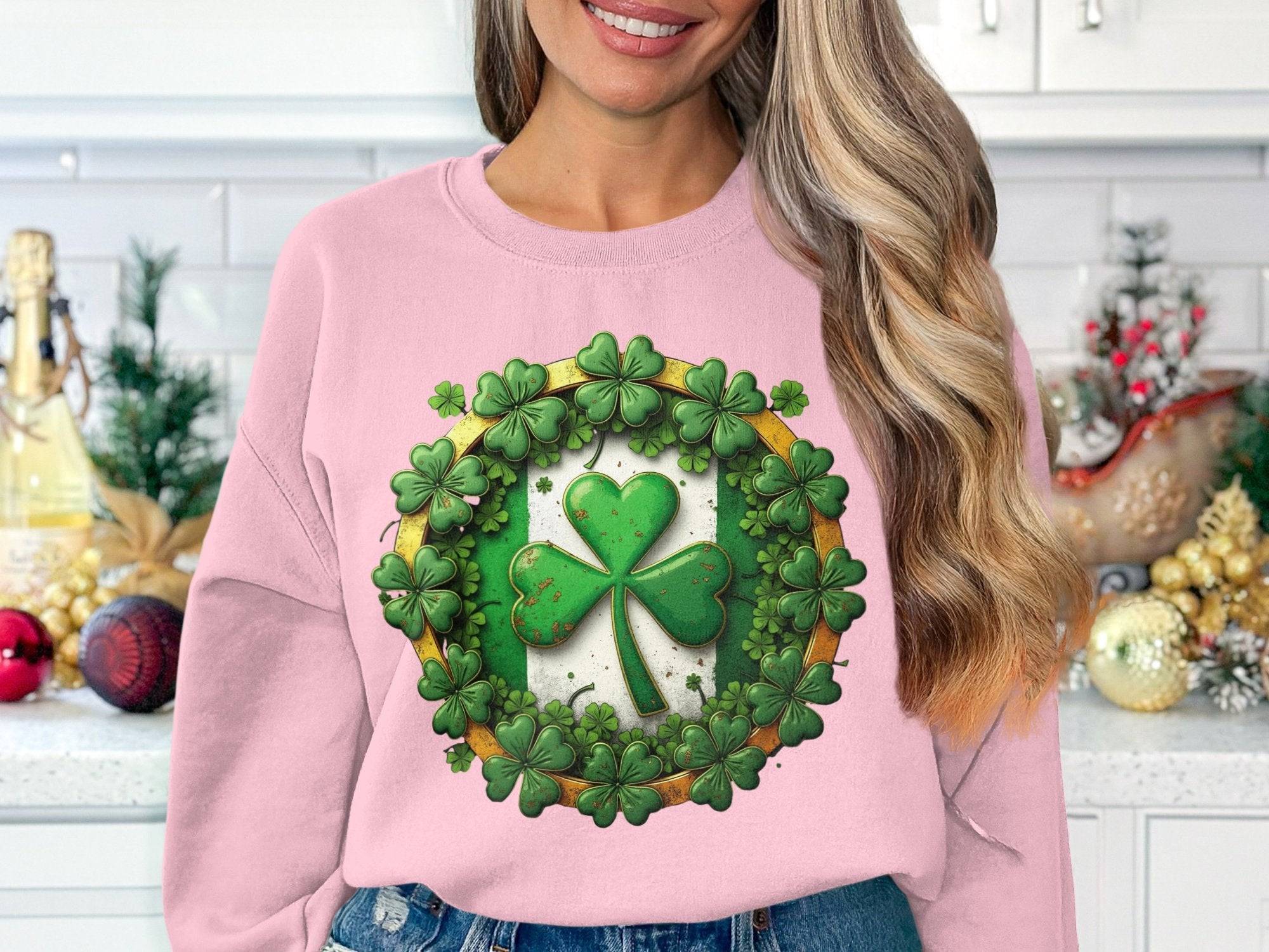 Amid festive kitchen decor, a woman showcases her Irish spirit with a pink Garment Graphics sweatshirt featuring a lucky four-leaf clover surrounded by smaller ones. Her long, wavy hair cascades as she smiles, savoring the charm of the moment.