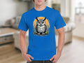 Someone is wearing a Garment Graphics blue T-shirt showcasing a detailed owl graphic with large eyes, featuring an orange circle and stylized foliage in the background, set in a cozy, blurred interior space.