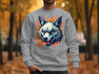 A person stands outdoors in a Garment Graphics gray wolf face sweatshirt, featuring an illustrated design that adds unique flair. The backdrop is an autumn scene with blurred trees and fallen leaves.