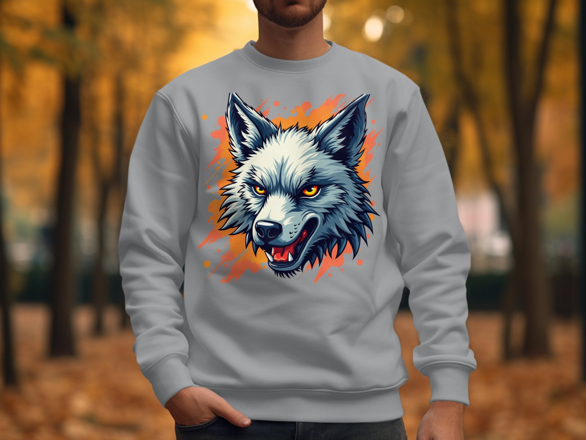 A person stands outdoors in a Garment Graphics gray wolf face sweatshirt, featuring an illustrated design that adds unique flair. The backdrop is an autumn scene with blurred trees and fallen leaves.