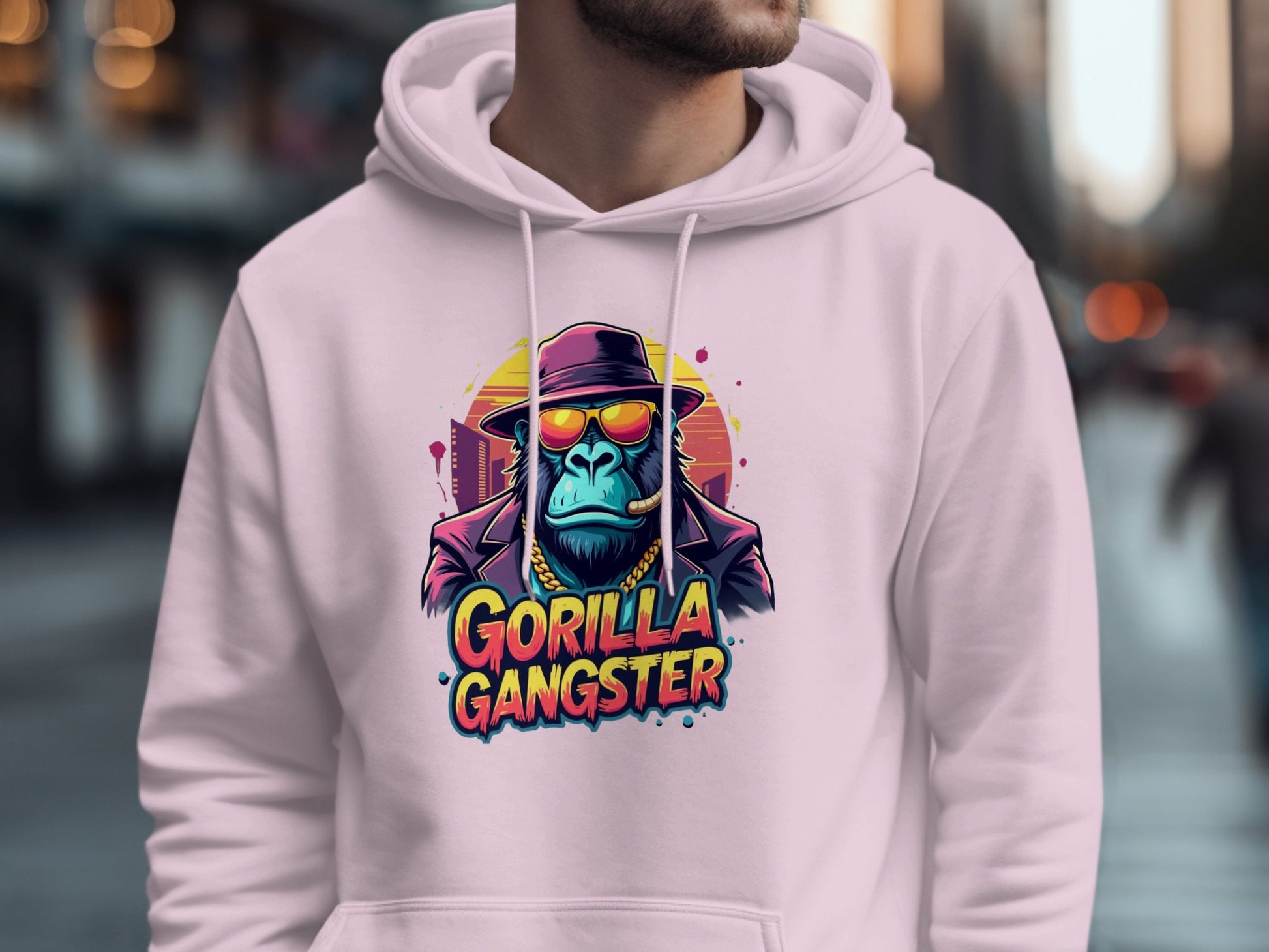 A person is wearing a white Garment Graphics hoodie from the Gangster Hoodies line, showcasing artwork of a blue sunglasses-wearing gorilla in a hat. The text Gorilla Gangster appears below, against a blurred streetwear-themed backdrop.