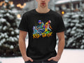 In a snowy setting, someone wears Garment Graphics black T-shirt featuring two skateboarders and the words Risk Taker, showcasing street dance culture against blurry snow-covered trees.