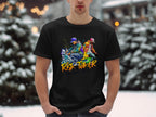 In a snowy setting, someone wears Garment Graphics black T-shirt featuring two skateboarders and the words Risk Taker, showcasing street dance culture against blurry snow-covered trees.