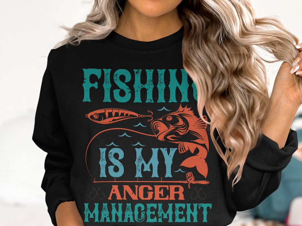 A person with long, wavy blonde hair wears a Garment Graphics sweatshirt featuring the vibrant turquoise and orange slogan Fishing Is My Anger Management. The design showcases a fish and fishing rod, ideal for fishing enthusiasts seeking peace on the water.