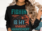 A person with long, wavy blonde hair wears a Garment Graphics sweatshirt featuring the vibrant turquoise and orange slogan Fishing Is My Anger Management. The design showcases a fish and fishing rod, ideal for fishing enthusiasts seeking peace on the water.