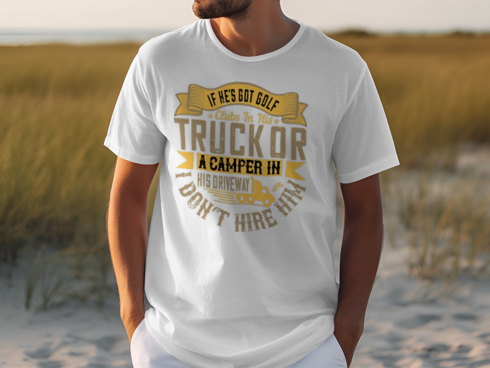 A person is wearing a white Garment Graphics T-shirt with gold and gray lettering that humorously states: If hes got golf clubs in his truck or a camper in his driveway, I dont hire him, standing outdoors amidst tall grass for a camping humor vibe.