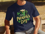 A person sports a Garment Graphics dark blue T-shirt featuring a Happy Patricks Day design with shamrocks and a beer mug as they enjoy the festivities on an outdoor wooden bench.