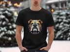 Outdoors in a snowy scene, an individual sports a Garment Graphics T-shirt showcasing a striking bulldog design with a spiked collar. Hands in pockets, they stand amidst snow-laden trees and blurred lights.