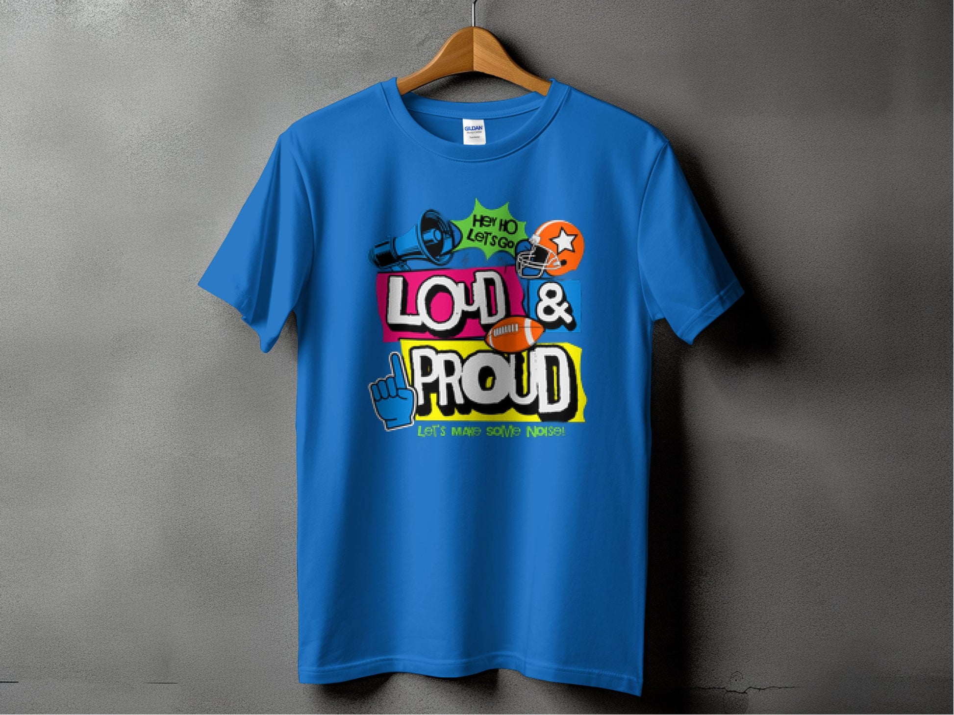 A Garment Graphics blue T-shirt hangs on a plain gray wall, featuring megaphones, stars, and colorful text: Loud & Proud and Lets Make Some Noise! Ideal for football enthusiasts to showcase their passion.