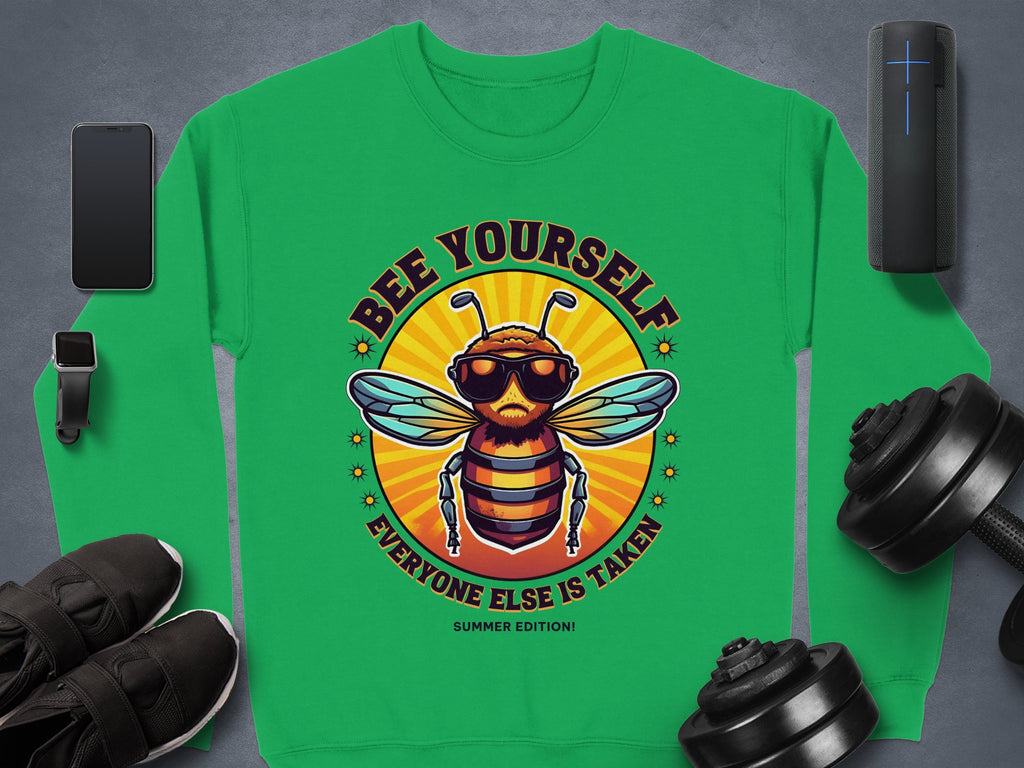 Garment Graphics presents a green sweatshirt with a cartoon bee in sunglasses and the quote Bee Yourself, Everyone Else is Taken. Part of the Summer Edition Sweatshirts collection, its available in unisex sizes. Featured with it are a smartphone, smartwatch, sneakers, dumbbells, and speaker.