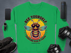 Garment Graphics presents a green sweatshirt with a cartoon bee in sunglasses and the quote Bee Yourself, Everyone Else is Taken. Part of the Summer Edition Sweatshirts collection, its available in unisex sizes. Featured with it are a smartphone, smartwatch, sneakers, dumbbells, and speaker.