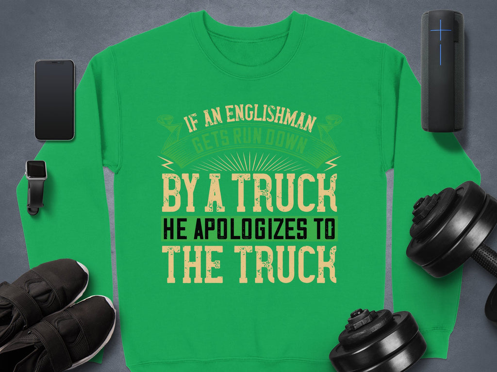Garment Graphics offers a unisex green sweatshirt with a bold, humorous design: If an Englishman gets run down by a truck, he apologizes to the truck. Its displayed on a gray surface surrounded by a smartphone, smartwatch, portable speaker, shoes, and dumbbells.