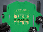 Garment Graphics offers a unisex green sweatshirt with a bold, humorous design: If an Englishman gets run down by a truck, he apologizes to the truck. Its displayed on a gray surface surrounded by a smartphone, smartwatch, portable speaker, shoes, and dumbbells.