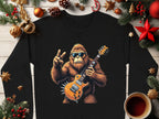 The Garment Graphics black shirt showcases Bigfoot with sunglasses, an electric guitar, and a peace sign among Christmas decorations like fir branches, ornaments, candy canes, and coffee. Its ideal for music lovers who cherish the holiday spirit.