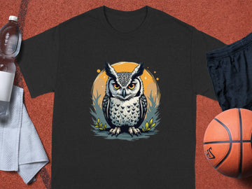 Garment Graphics black T-shirt features a stern owl graphic standing on grass against an orange circular background. Perfect for sporty vibes, its styled with a water bottle, towel, black athletic shorts, and a basketball on a flat surface.