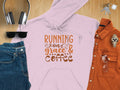 A flat lay features the Running on Grace and Coffee hoodie by Garment Graphics, made of medium-heavy fabric for a comfy classic fit. Surrounding the pink hoodie are black headphones, sunglasses, denim pants, a brown shirt, a wristwatch, clear glasses, and keys.