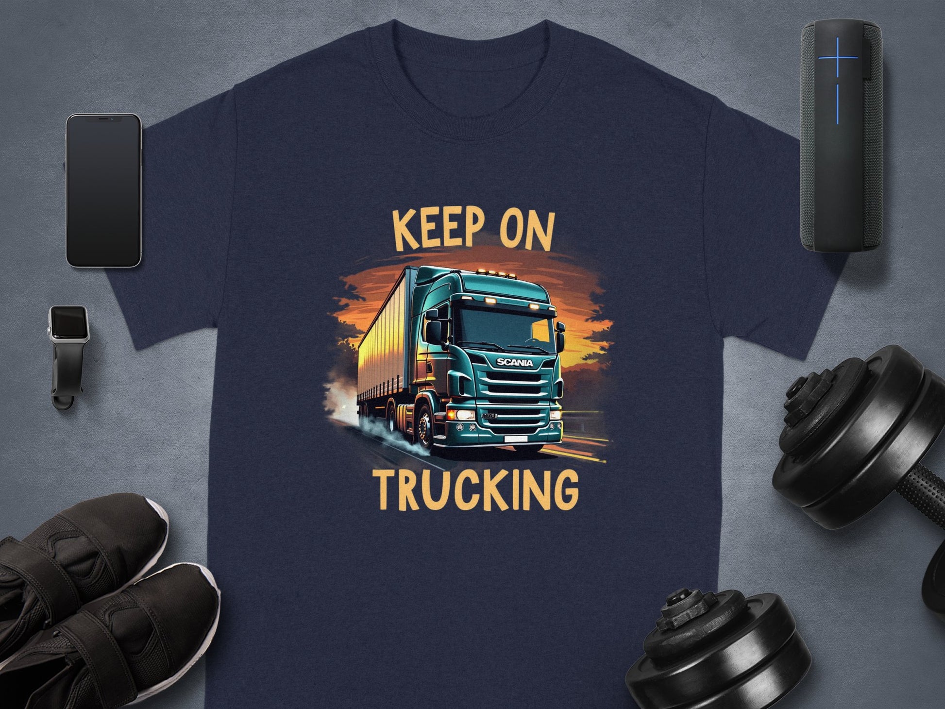 This Garment Graphics navy blue graphic T-shirt is ideal for truck enthusiasts, featuring a bold illustration of a large truck with the text Keep On Trucking above and below. Pair it seamlessly with a smartwatch, smartphone, wireless speaker, sneakers, and a dumbbell.