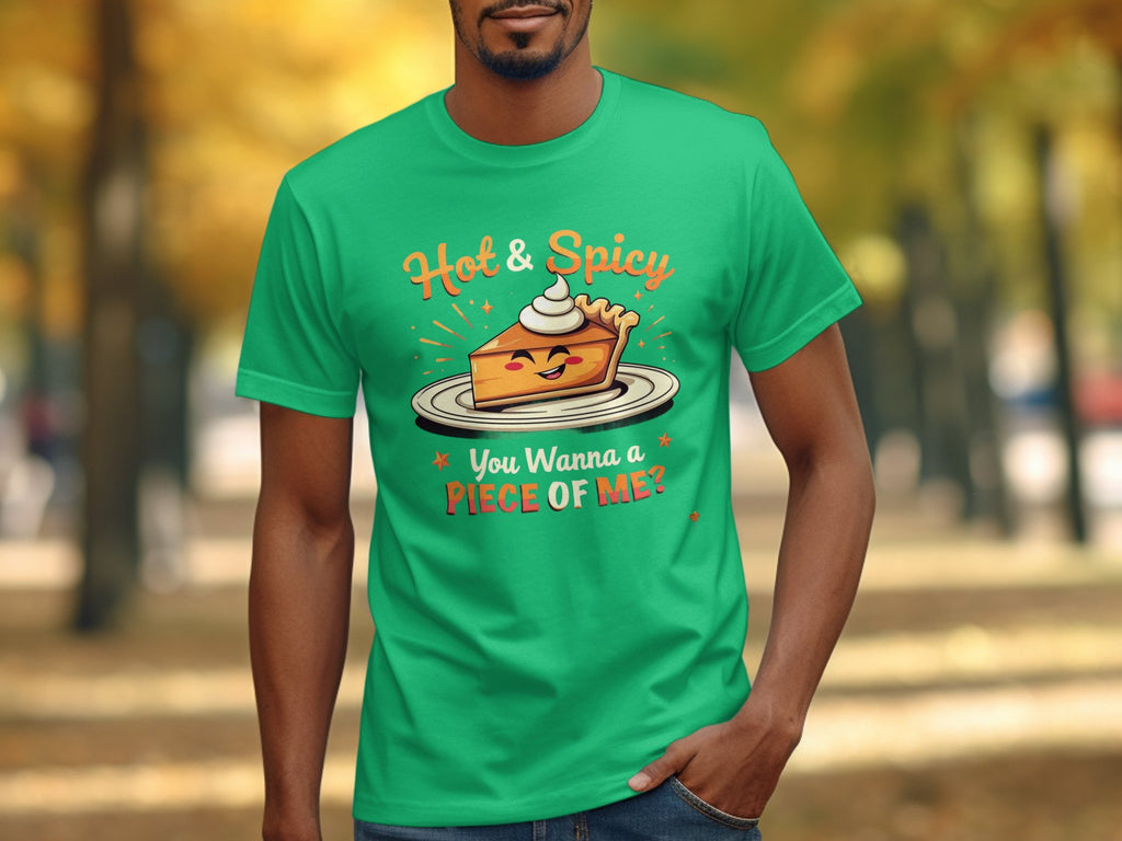 In a park with blurred autumn trees, someone wears a green Garment Graphics t-shirt featuring a winking pie slice topped with cream, boldly stating Hot & Spicy, You Wanna a Piece of Me? Perfect for grabbing attention and suitable for the whole family.