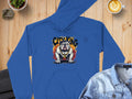 Garment Graphics blue hoodie features a fierce bulldog design surrounded by flames and the text CITY KING, styled with urban edge. Displayed on a wooden surface, its paired with a denim jacket, latte, and plant.