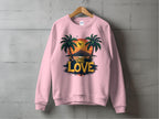 Garment Graphics One Love Sweatshirts collection features a unisex pink sweatshirt on a wooden hanger. It displays a sunset graphic with palm trees and birds, and ONE LOVE in bold yellow and black, set against a textured gray wall backdrop.