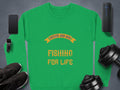 Garment Graphics vintage sweatshirts feature a green design with Father and Son Fishing for Life in yellow. Nearby on the gray surface are a smartphone, smartwatch, wireless speaker, black sneakers, and dumbbells.