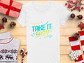 Amidst holiday-themed items like gifts and ornaments, a white T-shirt from Garment Graphics sits on a wooden surface, adorned with vibrant TAKE IT EASY graphics in blue and yellow, surrounded by musical notes and arrows—a perfect addition to the festive season.