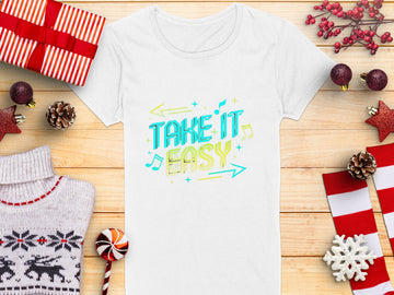 Amidst holiday-themed items like gifts and ornaments, a white T-shirt from Garment Graphics sits on a wooden surface, adorned with vibrant TAKE IT EASY graphics in blue and yellow, surrounded by musical notes and arrows—a perfect addition to the festive season.