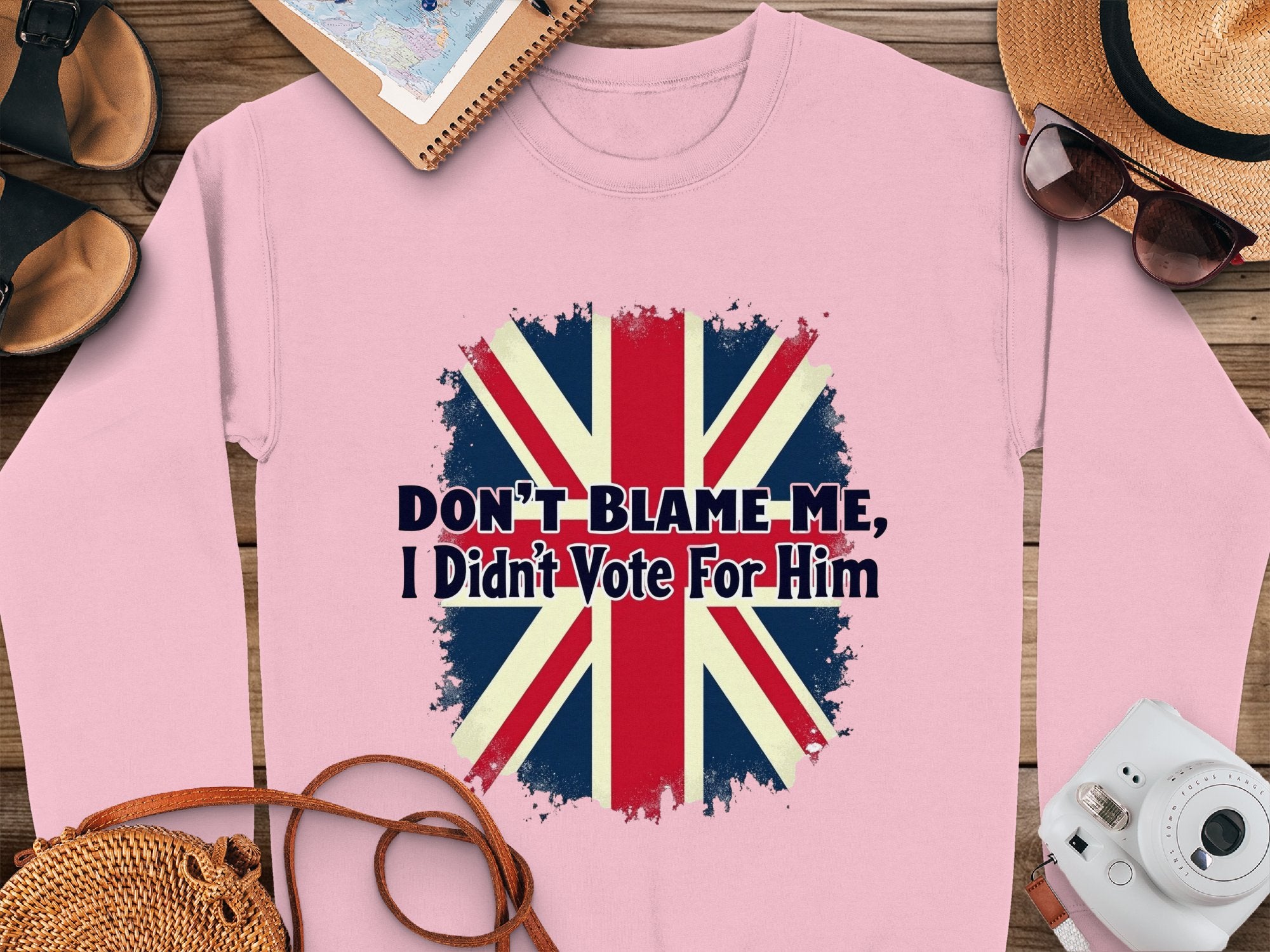 Garment Graphics pink unisex sweatshirt features a distressed Union Jack and Dont Blame Me, I Didnt Vote For Him text. Pair it with a straw hat, sunglasses, and stationery for a chic look.