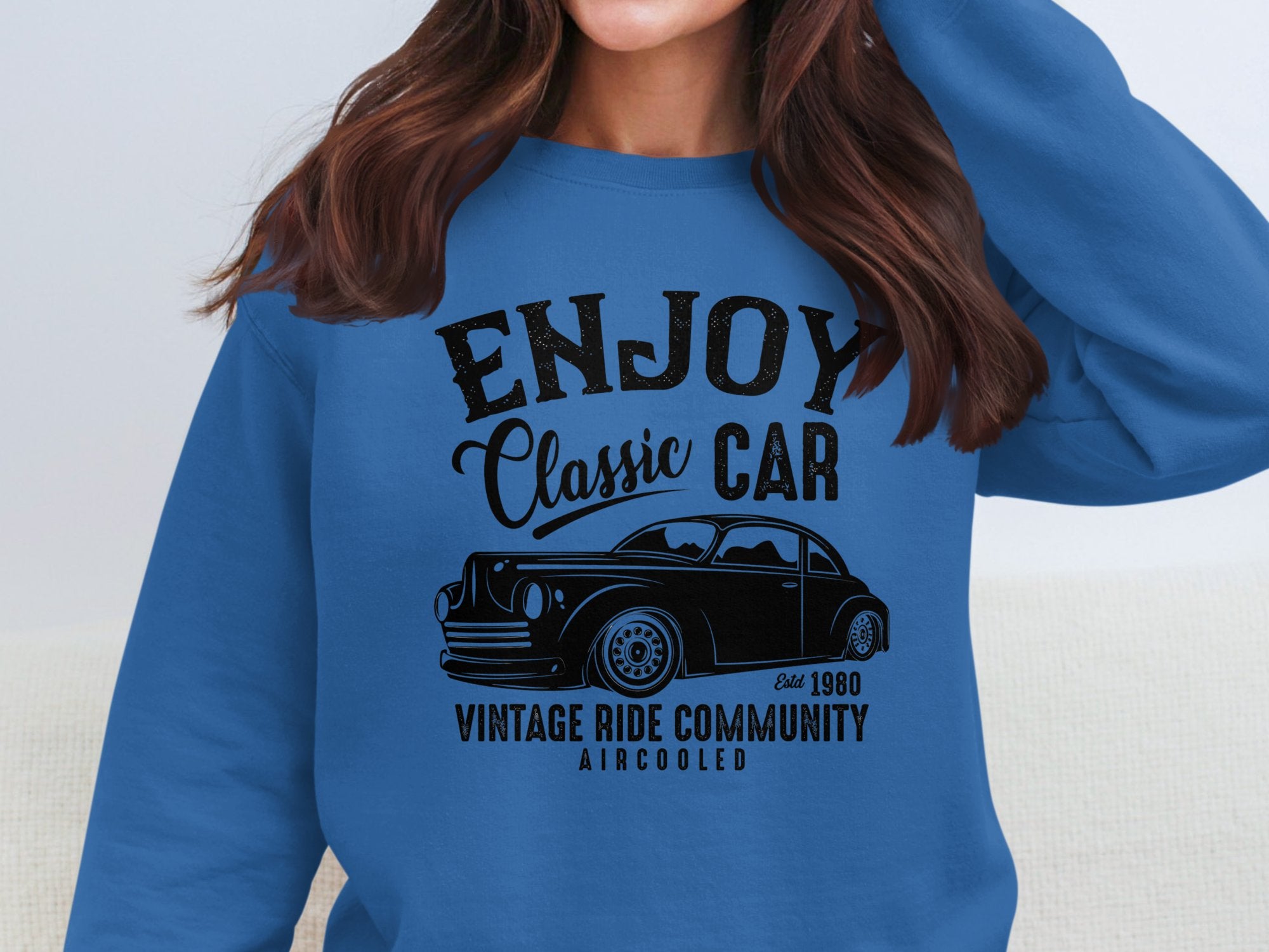 A person wears a blue sweatshirt from Garment Graphics featuring a black graphic of a classic car with the text Enjoy Vintage Ride, Classic Car Community, Aircooled, Est. 1980, while their face is not visible.