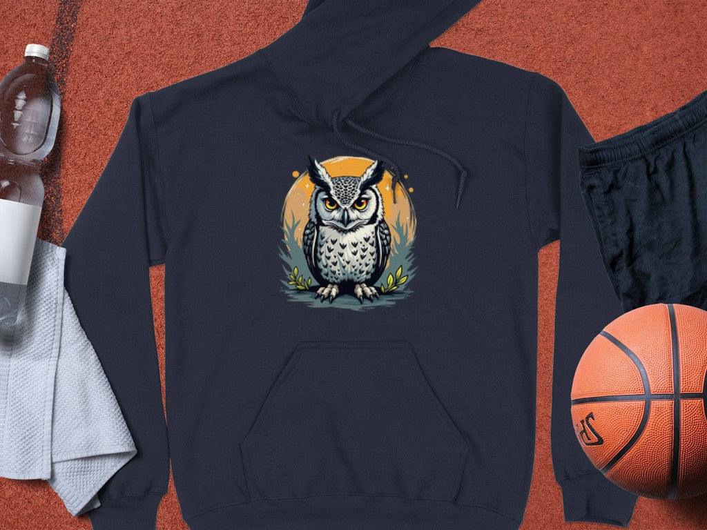 A medium-heavy fabric hoodie by Garment Graphics features an owl design on a dark gray backdrop with an orange circle, laid on a textured surface alongside a plastic water bottle, white towel, black shorts, and an orange basketball.