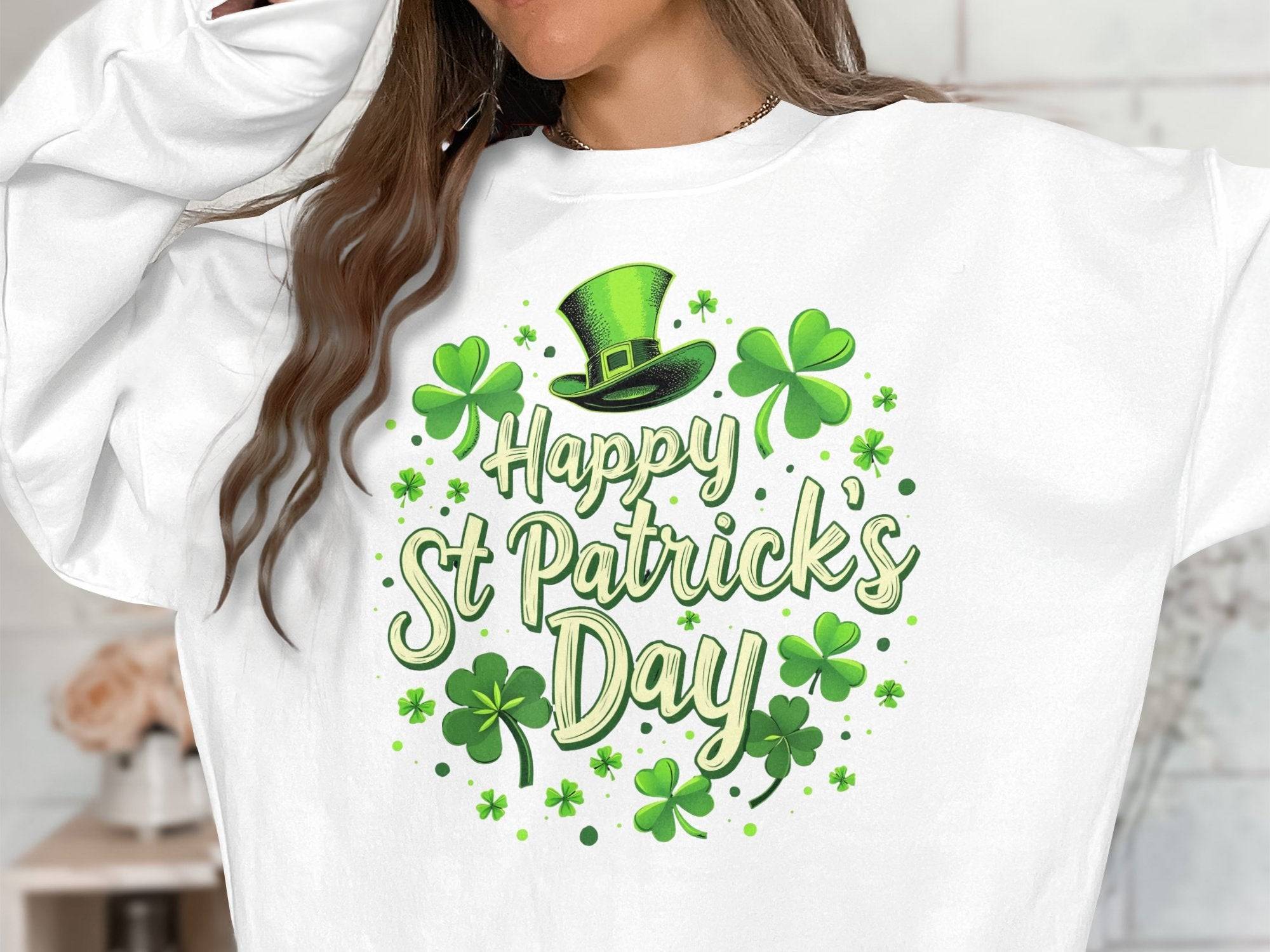 Clad in Garment Graphics white sweatshirt with a green Happy St Patricks Day print, shamrocks, and a leprechaun hat design, the person exudes festive cheer while playfully covering part of their face with one arm indoors.