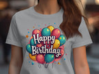 A person is wearing a vibrant 100% cotton t-shirt by Garment Graphics, featuring colorful balloons and Happy Birthday on the front. A softly blurred background enhances this joyful birthday celebration.