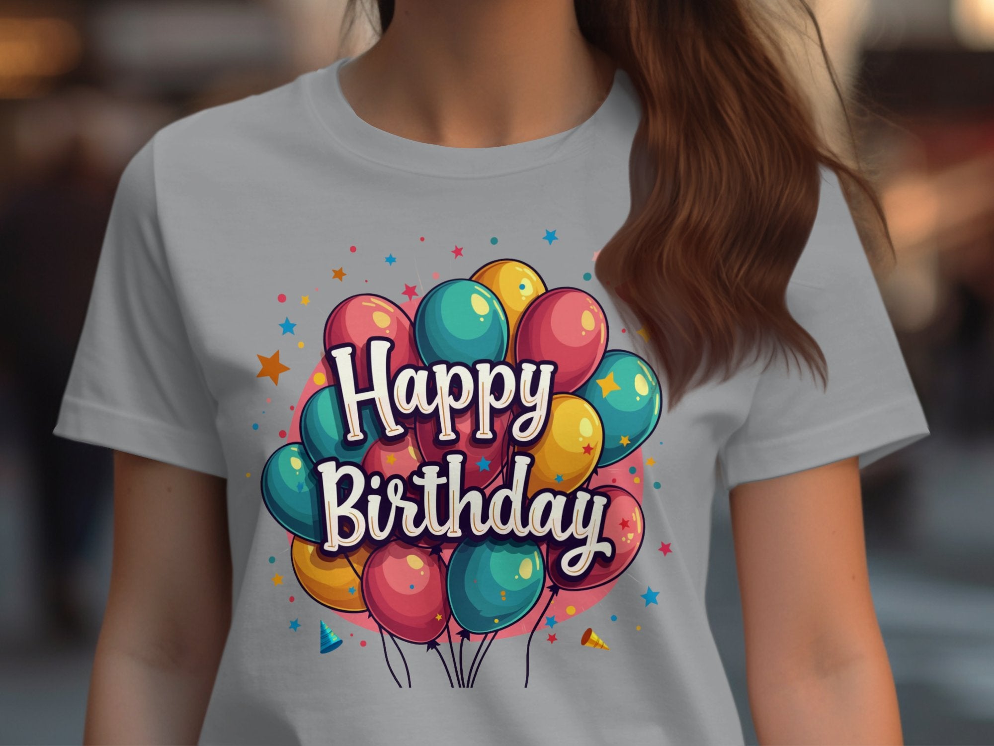 A person is wearing a vibrant 100% cotton t-shirt by Garment Graphics, featuring colorful balloons and Happy Birthday on the front. A softly blurred background enhances this joyful birthday celebration.
