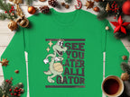 Garment Graphics offers a festive green unisex sweatshirt featuring a cartoon alligator with a basketball and playful See You Later Alligator text, surrounded by pine branches, ornaments, and a warm coffee cup for seasonal cheer.